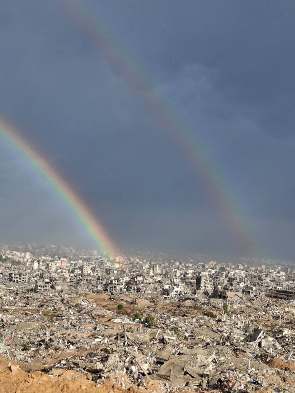 照片显示 - 加沙废墟上，晨雨过后出现彩虹。
